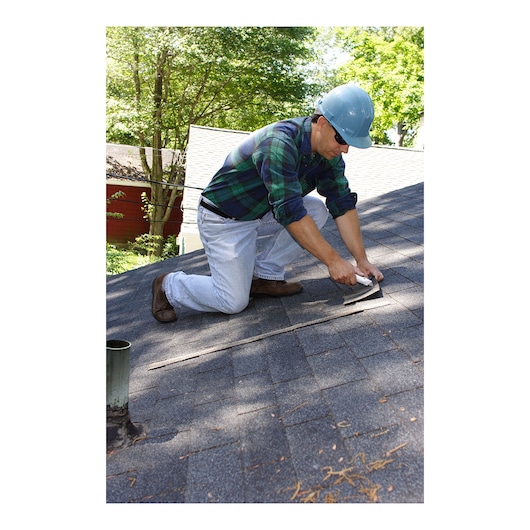 Photo of STANLEY 10-789 utility knife in use for rooftop shingle repair, person kneeling on gray roof.