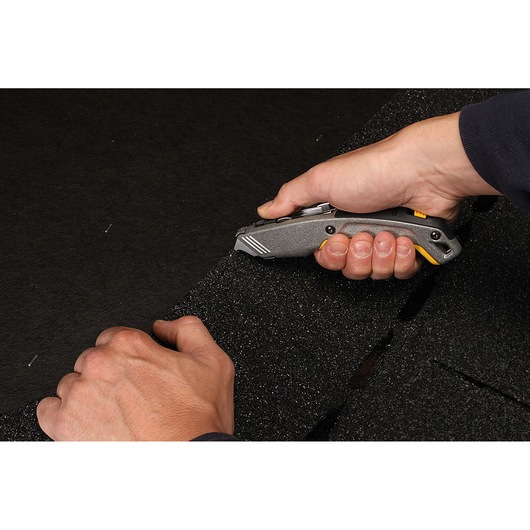 STANLEY 10-789 utility knife cutting thick black foam, handheld, close-up view.
