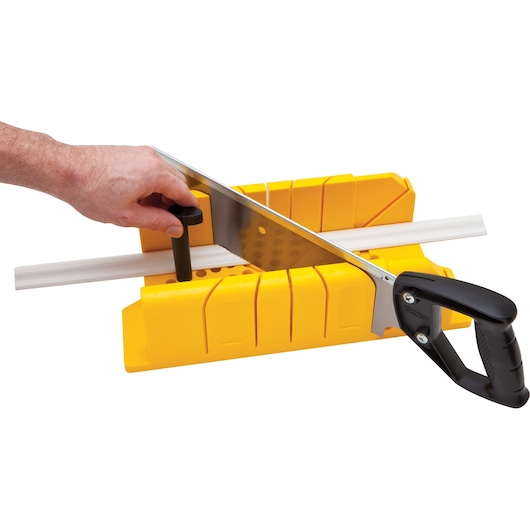 STANLEY 20-600 saw and yellow miter box cutting white molding, photography, side angle.