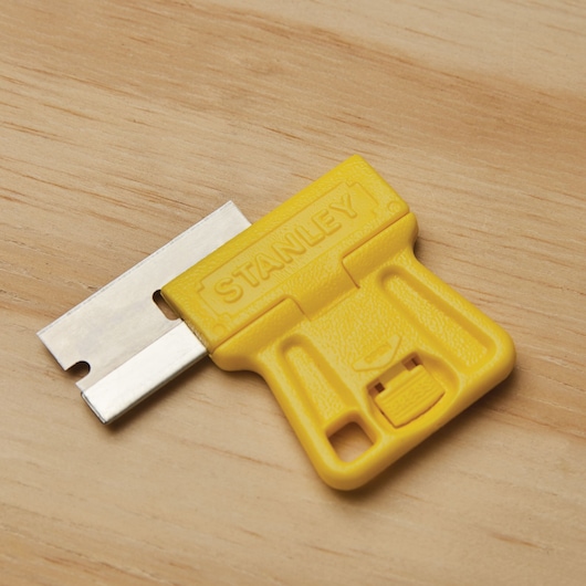 STANLEY 28-100 yellow plastic scraper with metal blade on a wood surface, close-up angle.