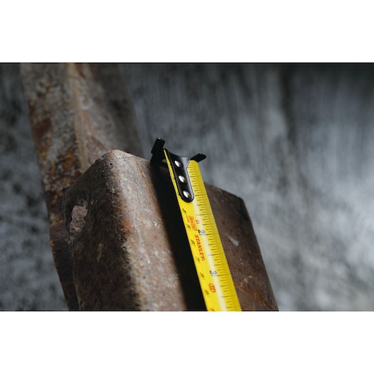 STANLEY 30-626 tape measure with yellow blade measuring a rough metal surface, close-up angle.
