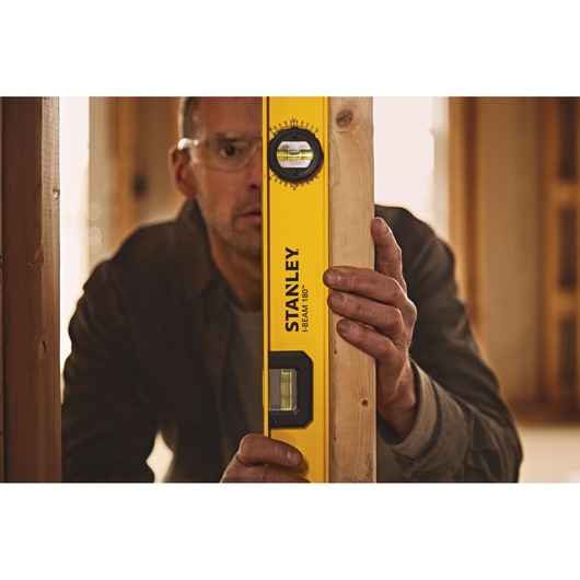 Photo of STANLEY 42-324 I-Beam 180° level tool being held against a wooden beam inside a construction site.