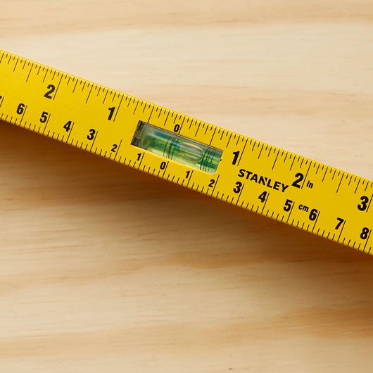 STANLEY 42-324 yellow measuring level with inch and centimeter markings, close-up angled on wood surface.