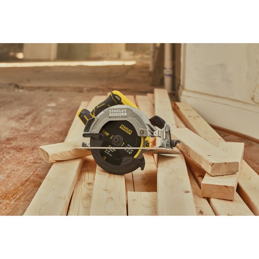 STANLEY SBC550 circular saw on wooden planks, side angle, black and yellow color, construction site.