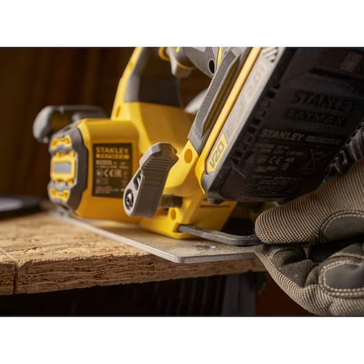 Stanley SBC550 power tool close-up, yellow cordless saw cutting wood, gloved hand adjusts base.