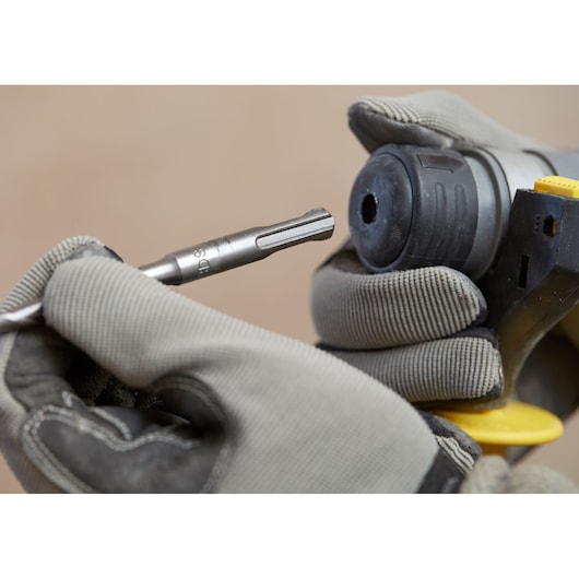 Stanley SBH900M2K-B3 drill bit being inserted into power tool, close-up photography of gloved hands.