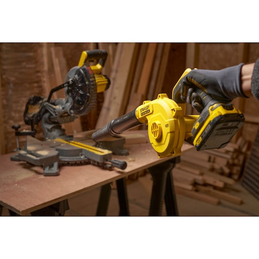 STANLEY SCBL01 cordless blower in use, close-up, yellow color, woodworking shop background, photography asset.