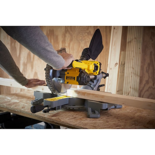 Stanley SCM701-B3 miter saw cutting wood on workbench, yellow and black color, side angle.