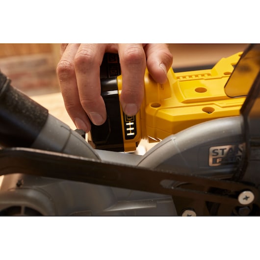 Stanley SCM701-B3 circular saw close-up showing battery installation with a hand holding the yellow tool.
