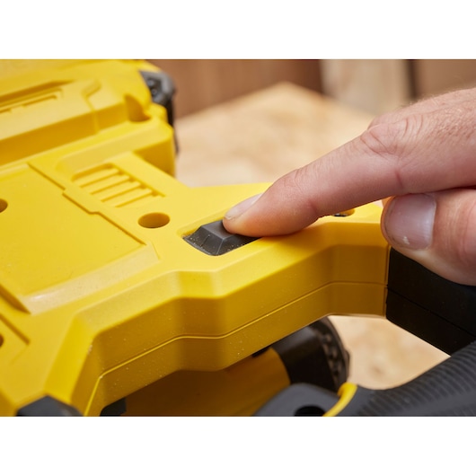 Photo of a hand pressing the power button on the yellow STANLEY SCM701-B3 power tool handle, close-up view.
