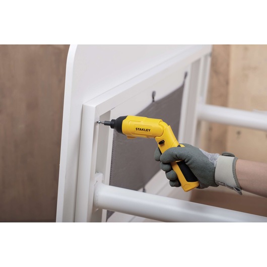 STANLEY SCS4K cordless screwdriver in use assembling white furniture, side angle.