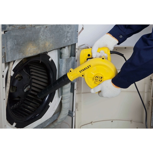 STANLEY SPT500-BR yellow electric blower used for cleaning a fan inside an appliance, close-up view.