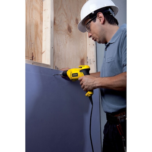 STANLEY STDR5206 corded drill used for drywall installation, side view, person wearing safety helmet.