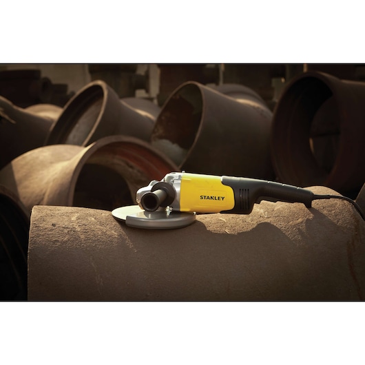 STANLEY STGL2223 angle grinder resting on large metal pipes, side view, yellow and black body.