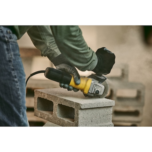 STANLEY stgs9115 angle grinder in use on concrete blocks, yellow and black tool held by gloved worker.