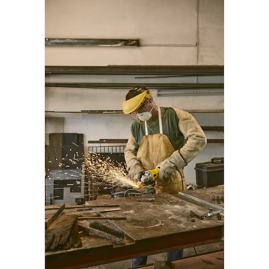 STANLEY stgs9115 photography of worker using yellow angle grinder with sparks in workshop, front angle.