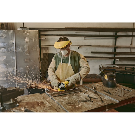 STANLEY stgs9115 photography of metalworker using yellow angle grinder, workbench with tools and sparks flying.