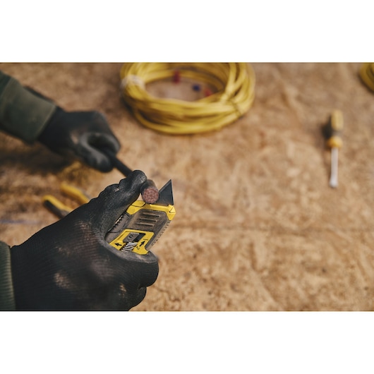 STANLEY STHT10432 utility knife cutting cable on workbench, worker in black gloves, coiled yellow wire and screwdriver nearby.