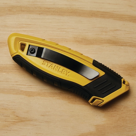 Photo of STANLEY STHT10432 utility knife, yellow and black, closed, shown on wood surface, side angle.