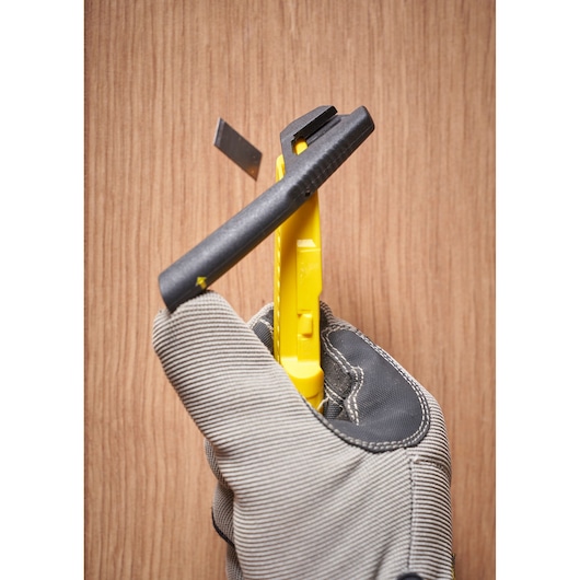 STANLEY STHT10489 yellow utility knife in a gloved hand, blade extended, close-up on wood background.