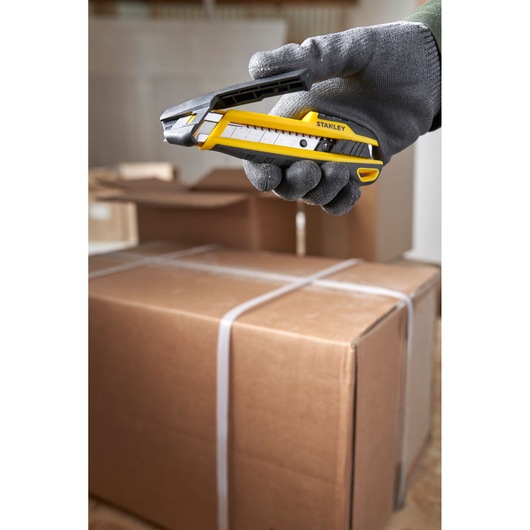 Photo of STANLEY STHT10501 utility knife held by gloved hand over cardboard boxes, side view.