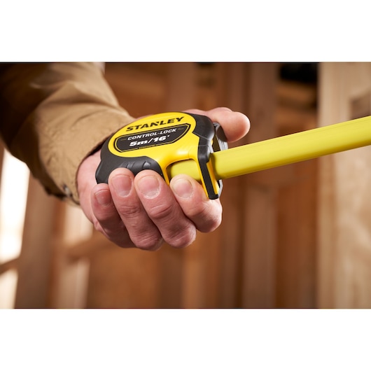 Photo of STANLEY STHT37246-0 tape measure with yellow and black casing, held in hand, extended in a workshop.