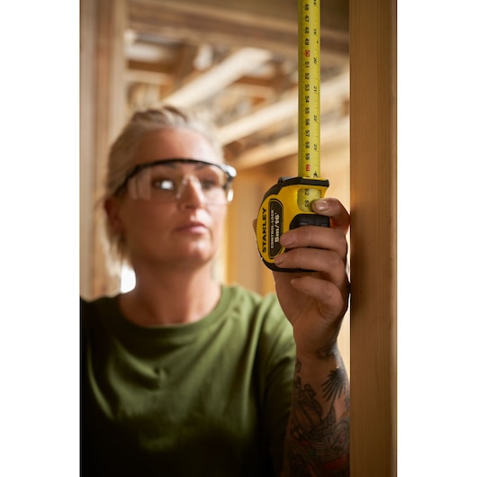 Photo of a person using STANLEY STHT37246-0 tape measure on a wooden frame, showing measurement in a construction setting.