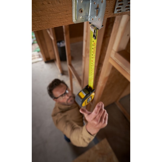 Photo of STANLEY STHT37247-0 tape measure extended vertically by a person, shown in a construction setting.