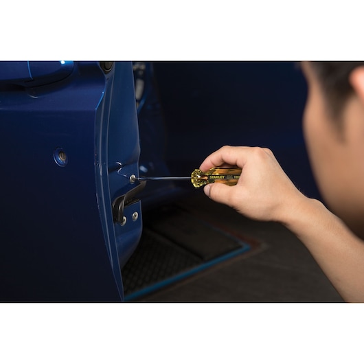 Stanley STHT69164 screwdriver in use on blue car door, close-up view, hand holding tool.