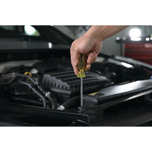 Photo of a hand using a STANLEY STHT69167 screwdriver on a car engine in a workshop setting.