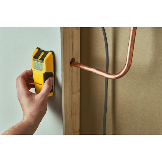 Photo of STANLEY STHT77406 stud finder detecting behind drywall, highlighting yellow handheld device.