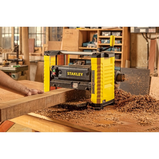 STANLEY STP18-B2 planer in use, yellow and black, wood shavings on workbench in workshop setting.