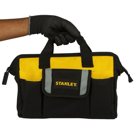 Stanley black and yellow tool bag held by a gloved hand, featuring multiple pockets and a zippered top.