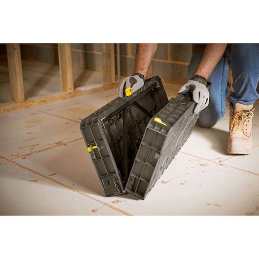 STANLEY STST83492-1 black plastic folding workbench being unfolded by gloved hands on job site floor.