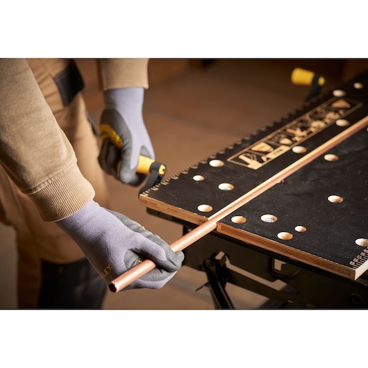 STANLEY STST83800-1 workbench photography showing gloved hands cutting copper pipe on black surface.