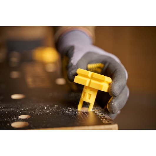 Photo of a gloved hand inserting a yellow STANLEY STST83800-1 workbench accessory into a black work surface.