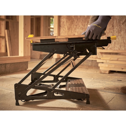 STANLEY STST83800-1 black folding workbench side angle, woodworking setup, construction background.
