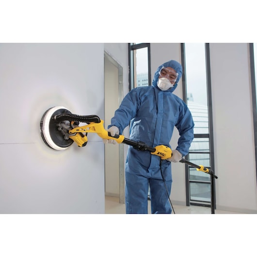 STANLEY SW75-BR drywall sander in use, yellow tool sanding wall, person in blue coveralls indoors.